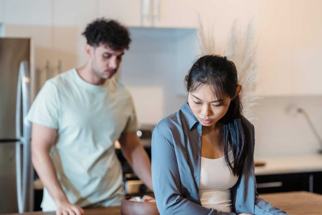 An Asian couple look dejected after an argument in the kitchen.