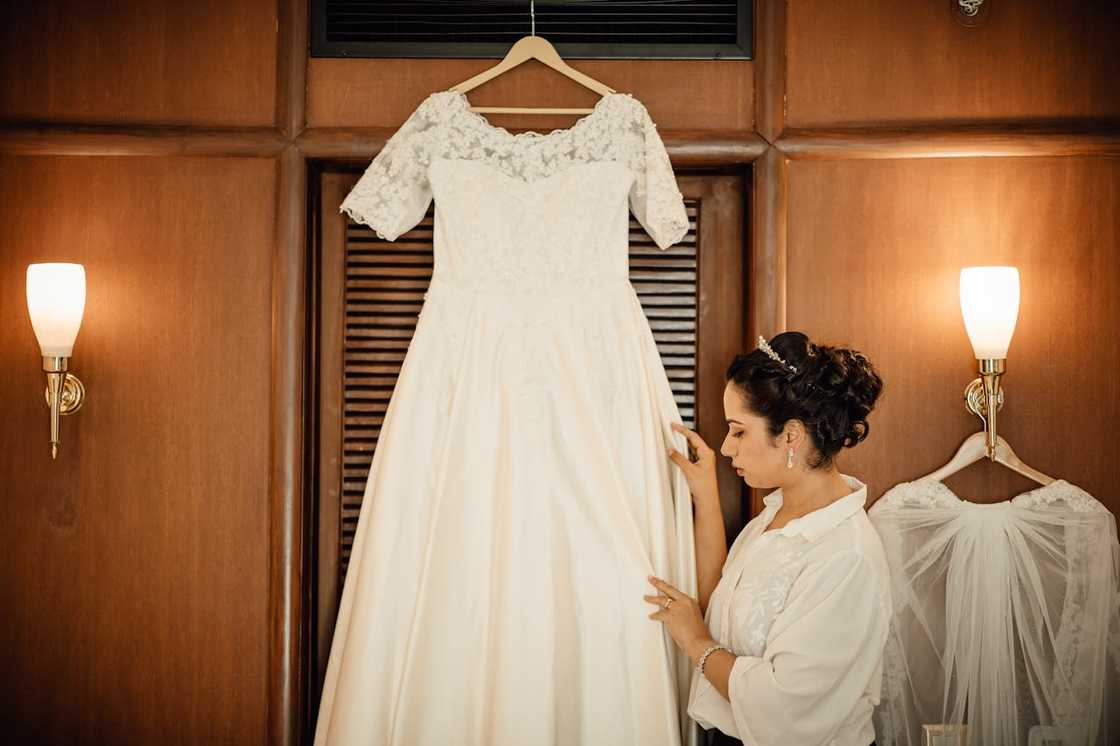 Bride adjusting a white wedding dress hanging in a dressing room.
