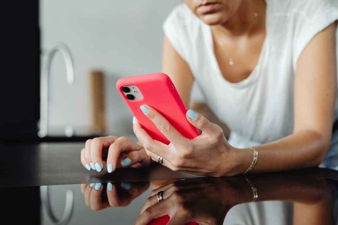A woman wearing glasses looks down at her phone while standing against a light wooden wall. A woman wearing glasses looks down at her phone while standing against a light wooden wall.