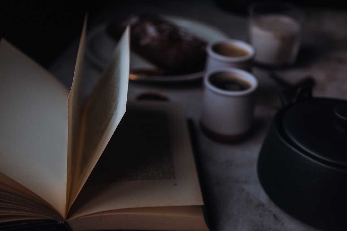 A nighttime reading scene with an open book with coffee cups on a desk.