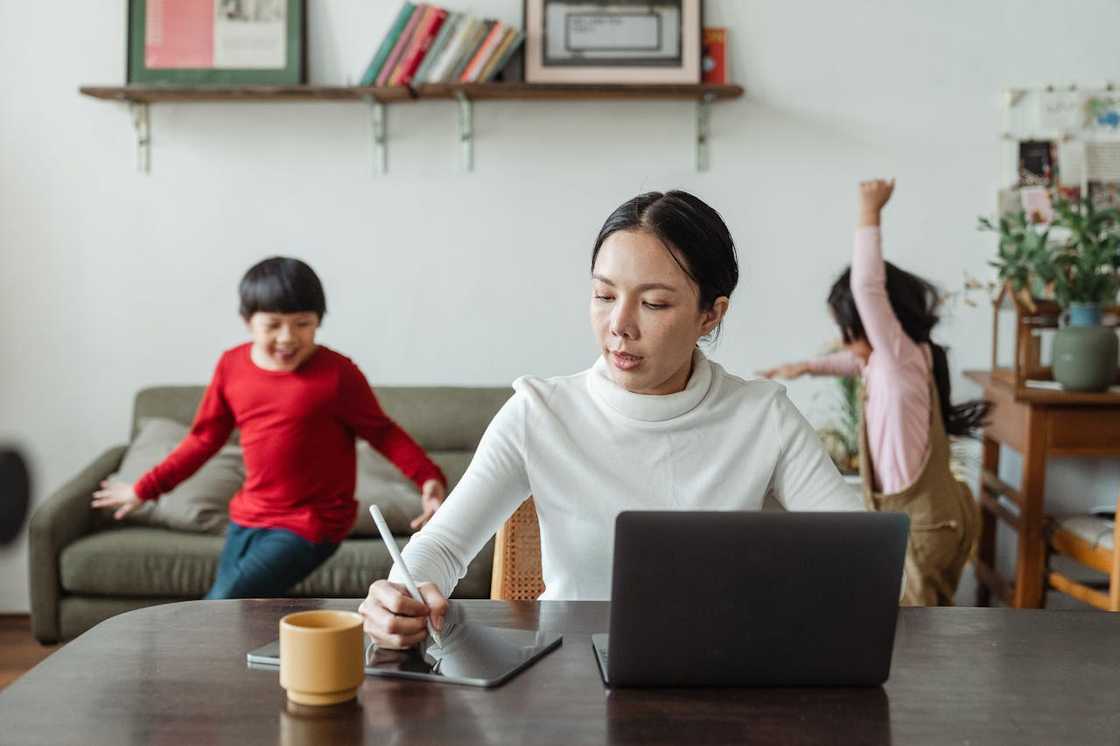 A mother sketches ideas while the children play in the background.