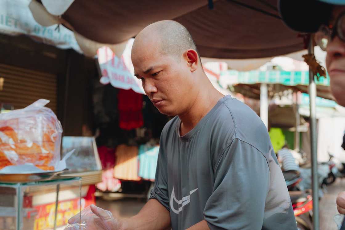 A middle-aged man sitting in a busy outdoor market stall.