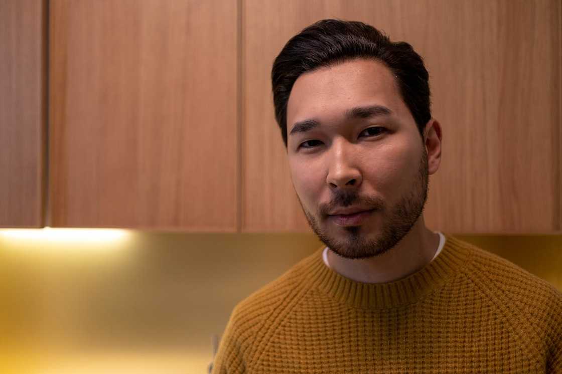 A man in a yellow sweater reflects alone at home.