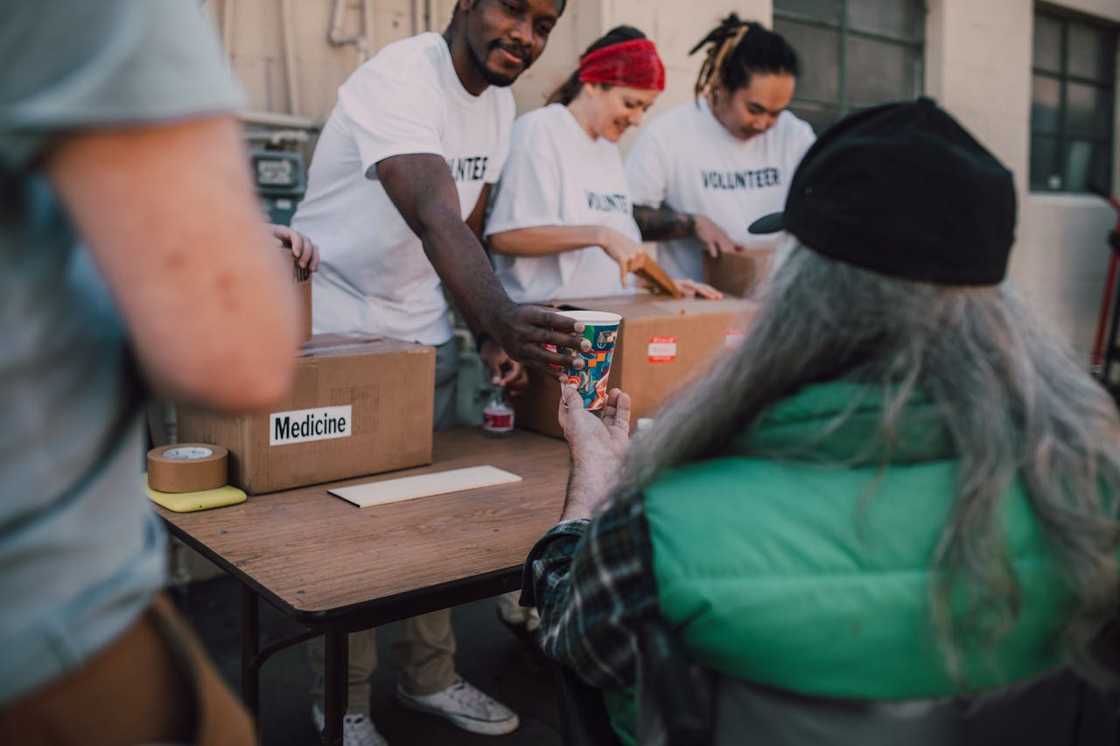 A group of volunteers handing a food cup to an older person during a community aid distribution. A group of volunteers handing a food cup to an older person during a community aid distribution.