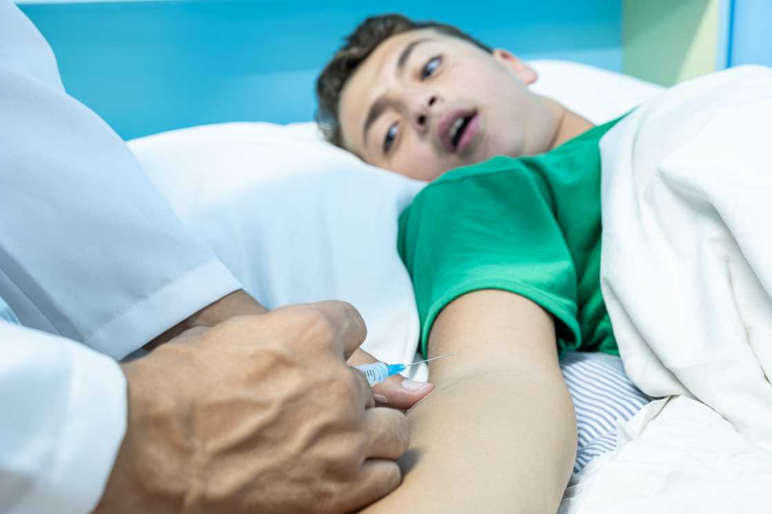 A teen boy on a hospital bed, doctors administering medicine