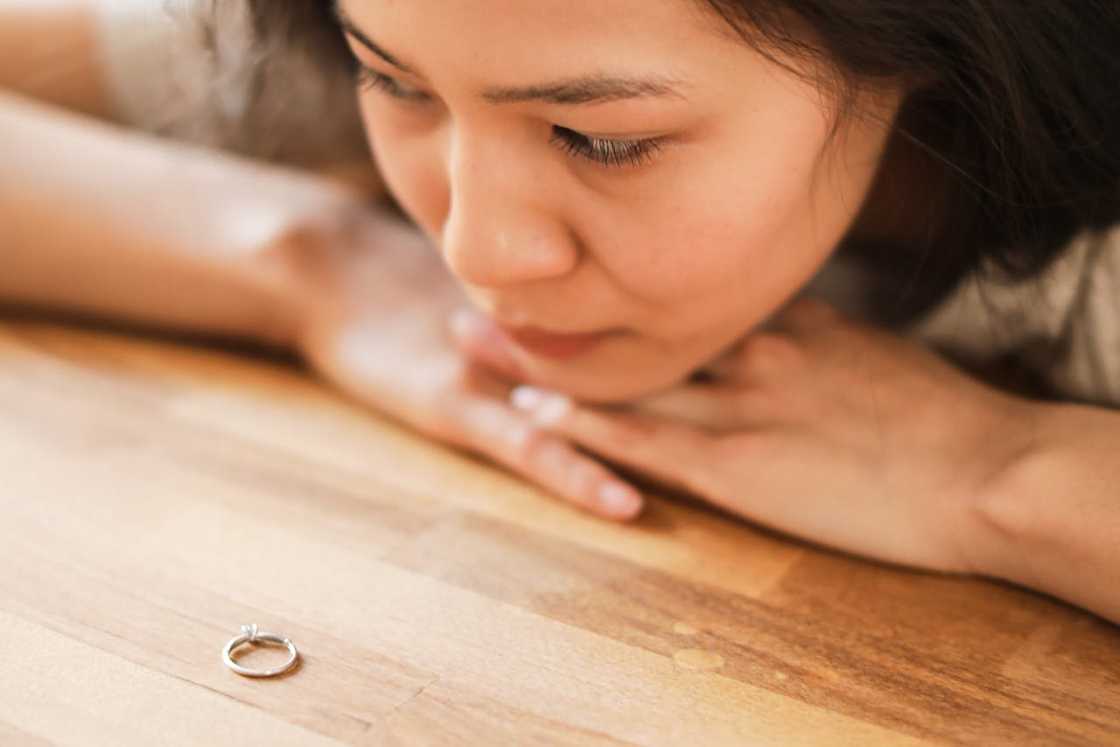 A woman gazing at a ring placed on a wooden table.
