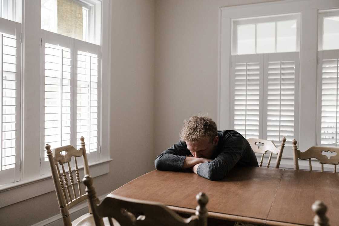 A person rests his head on folded arms at a dining table.