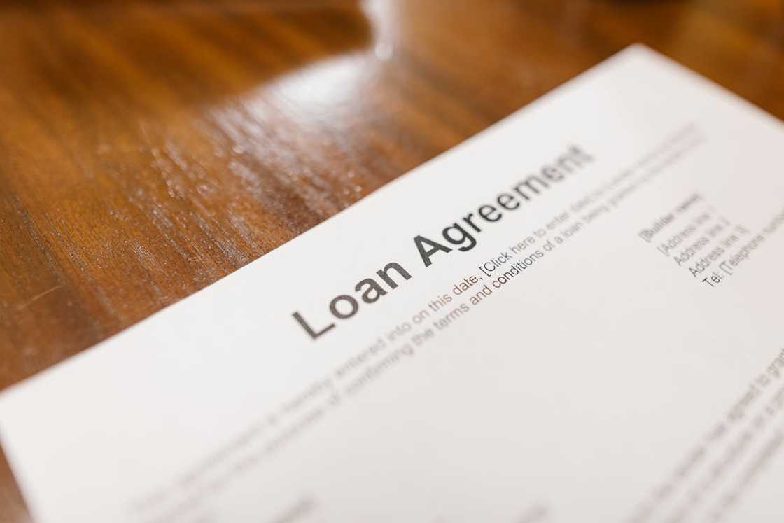 A loan agreement document lies on a wooden table. A loan agreement document lies on a wooden table.