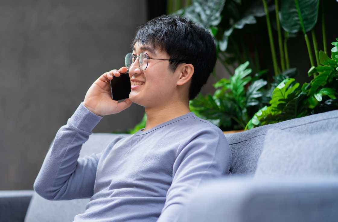 A young man smiling while using phone at at home