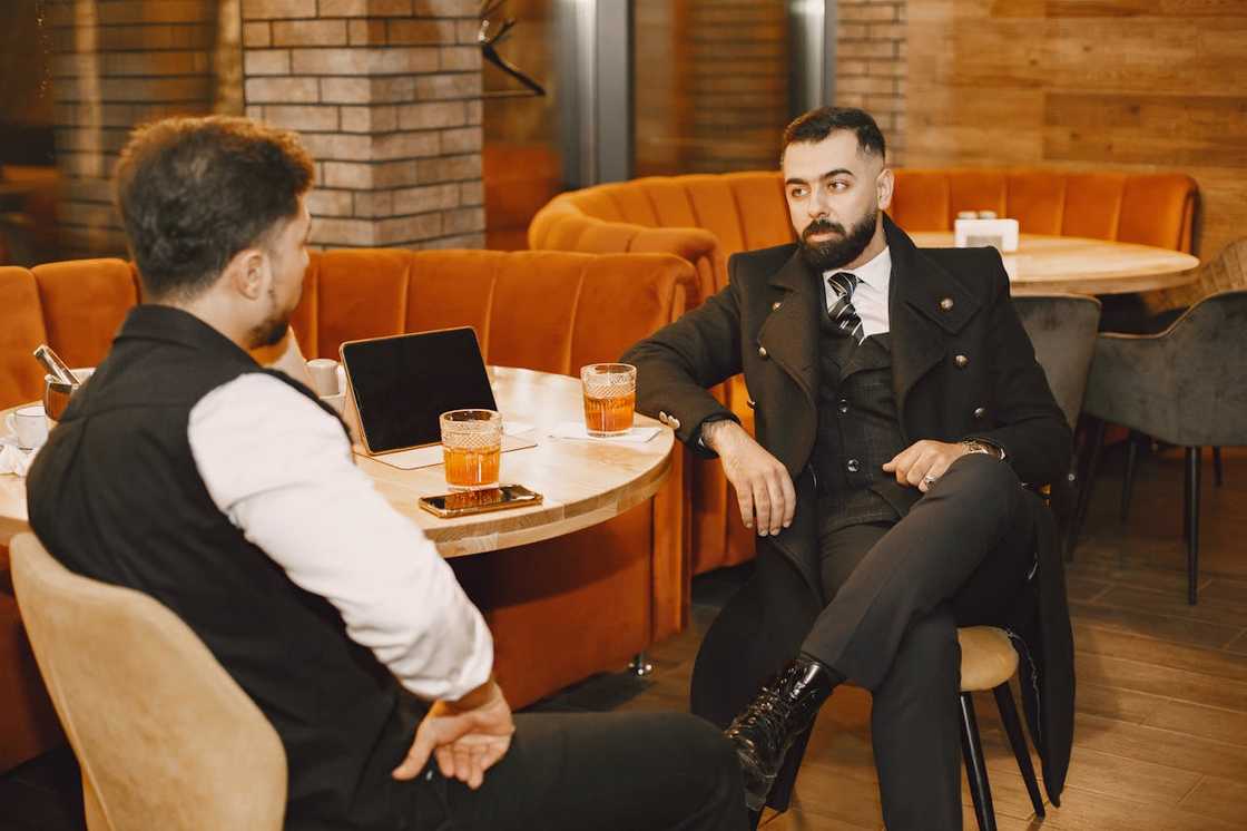 Two men talk at a table in a café over drinks. Two men talk at a table in a café over drinks.