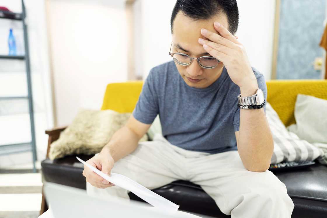 A man staring at a document while sitting on the sofa