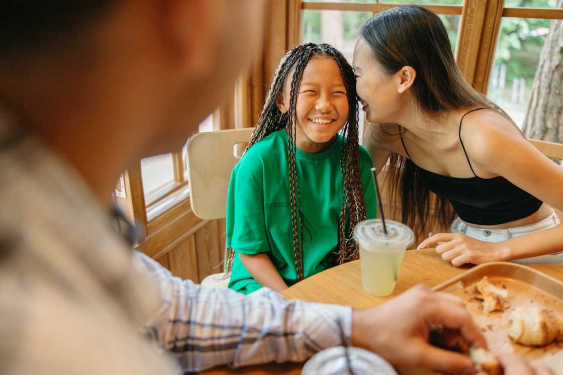 Three people share drinks and pastries at a sunlit wooden table, smiling and chatting warmly. Three people share drinks and pastries at a sunlit wooden table, smiling and chatting warmly.