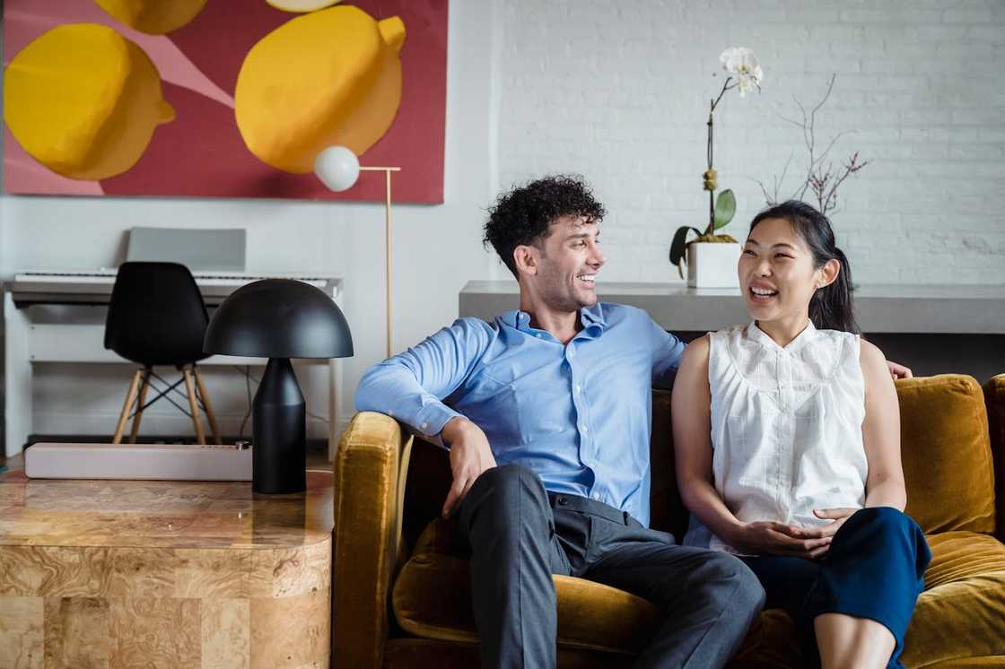 A man and woman sit on a sofa, smiling and talking.